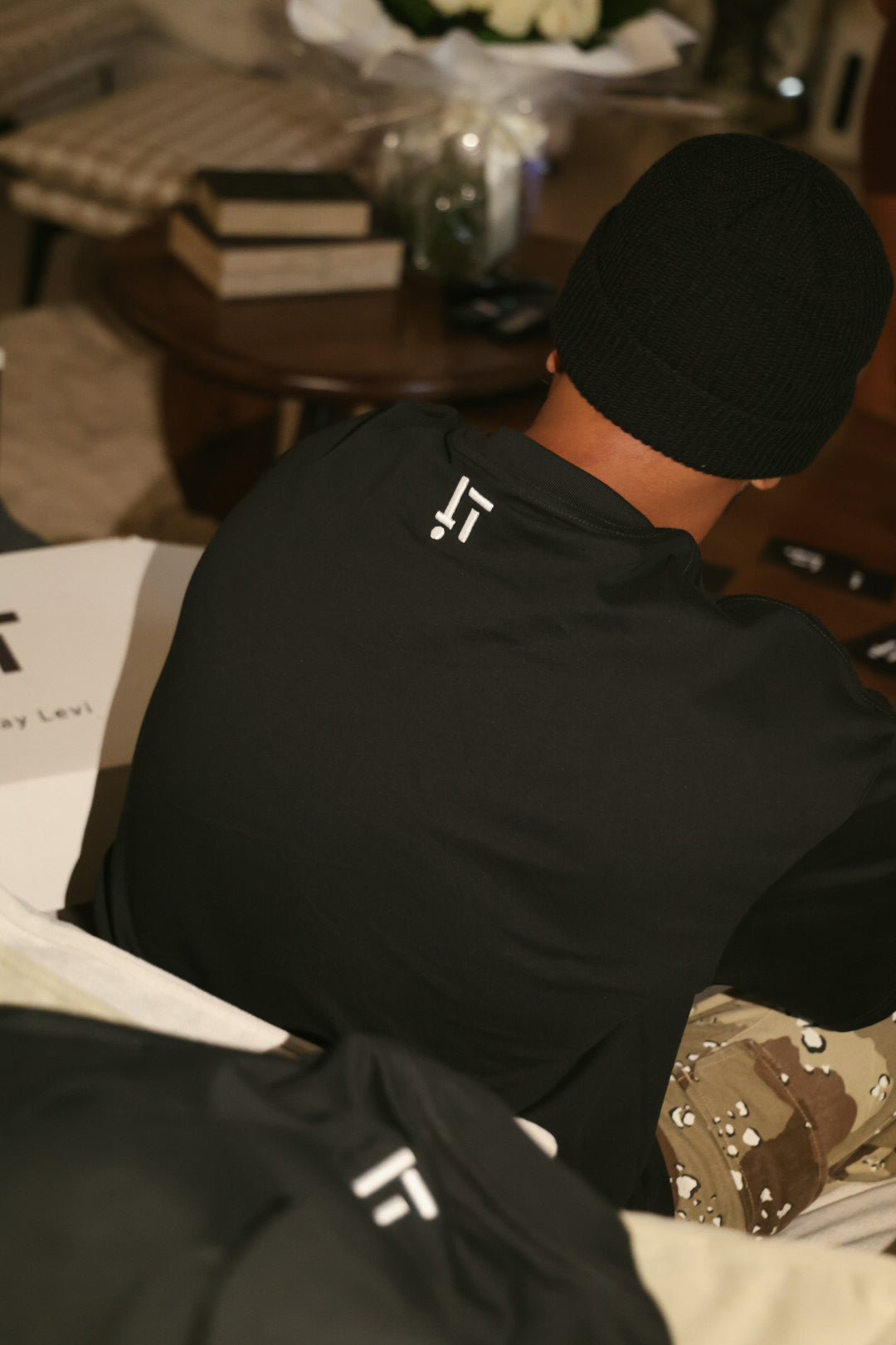 Itay Levi wearing a black hoodie with a logo, sitting on a couch.