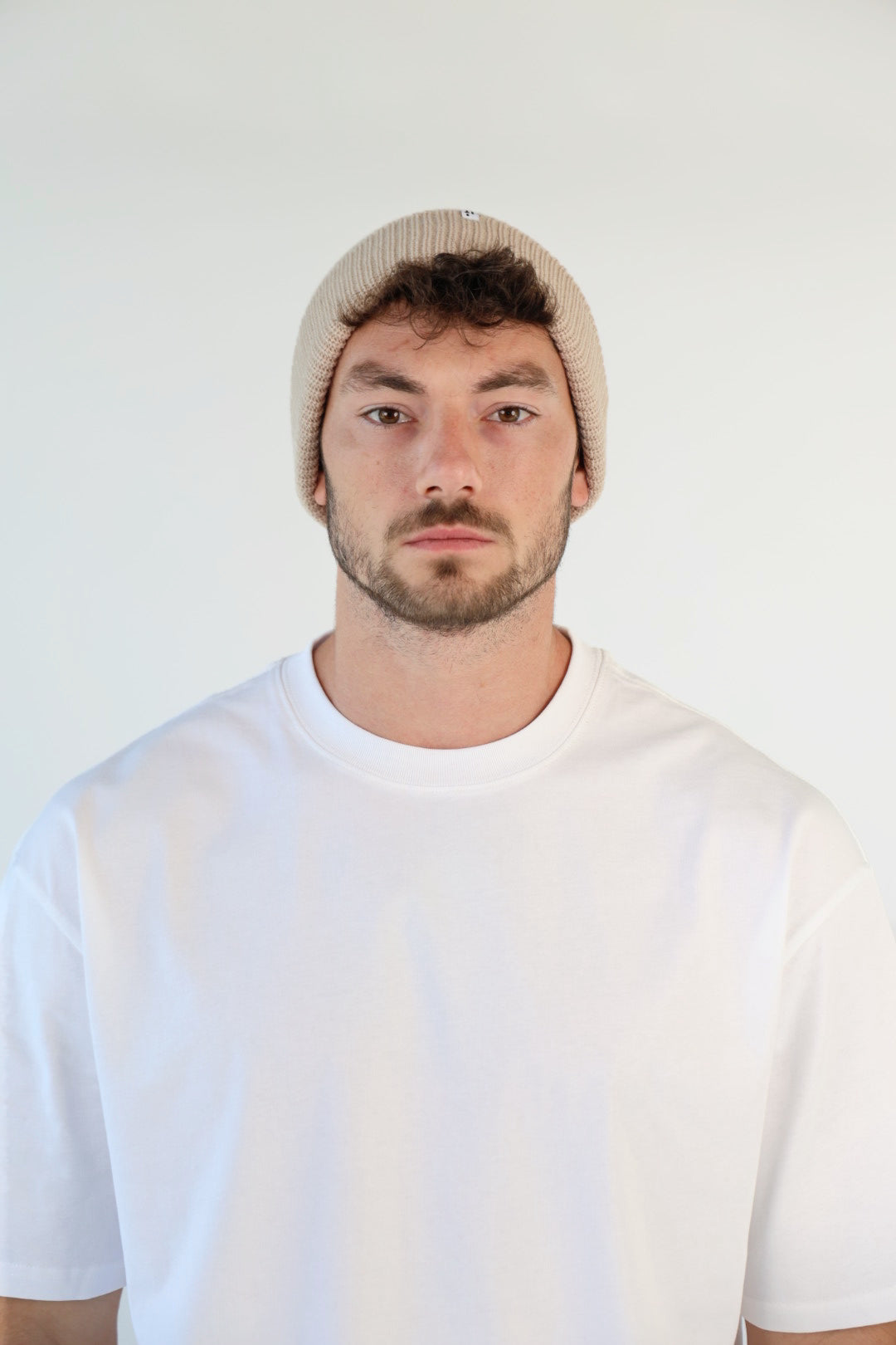 Man wearing a beige beanie and white t-shirt against a plain background