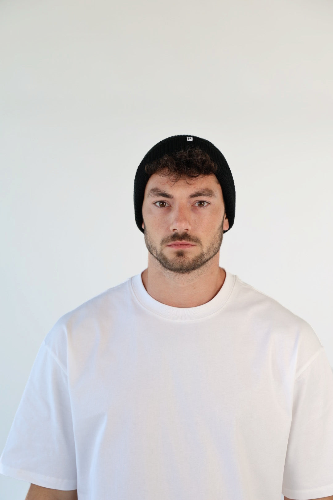 Man wearing a black beanie and white t-shirt against a plain background