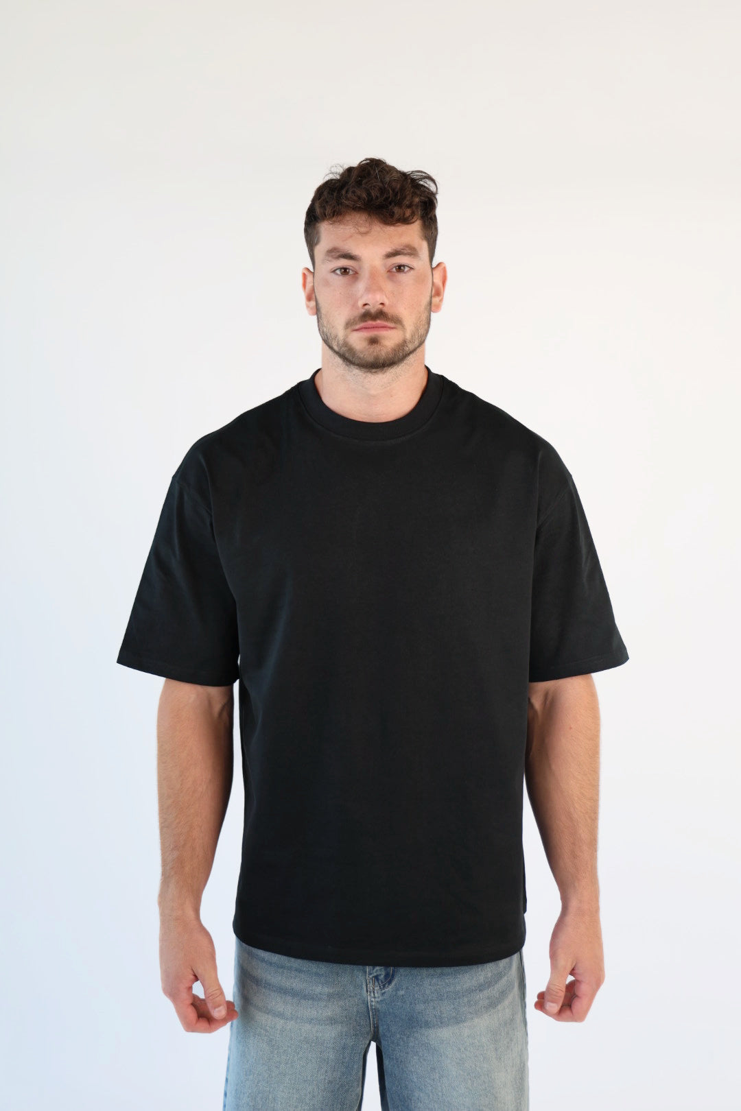 Man wearing a black t-shirt and light blue jeans against a white background
