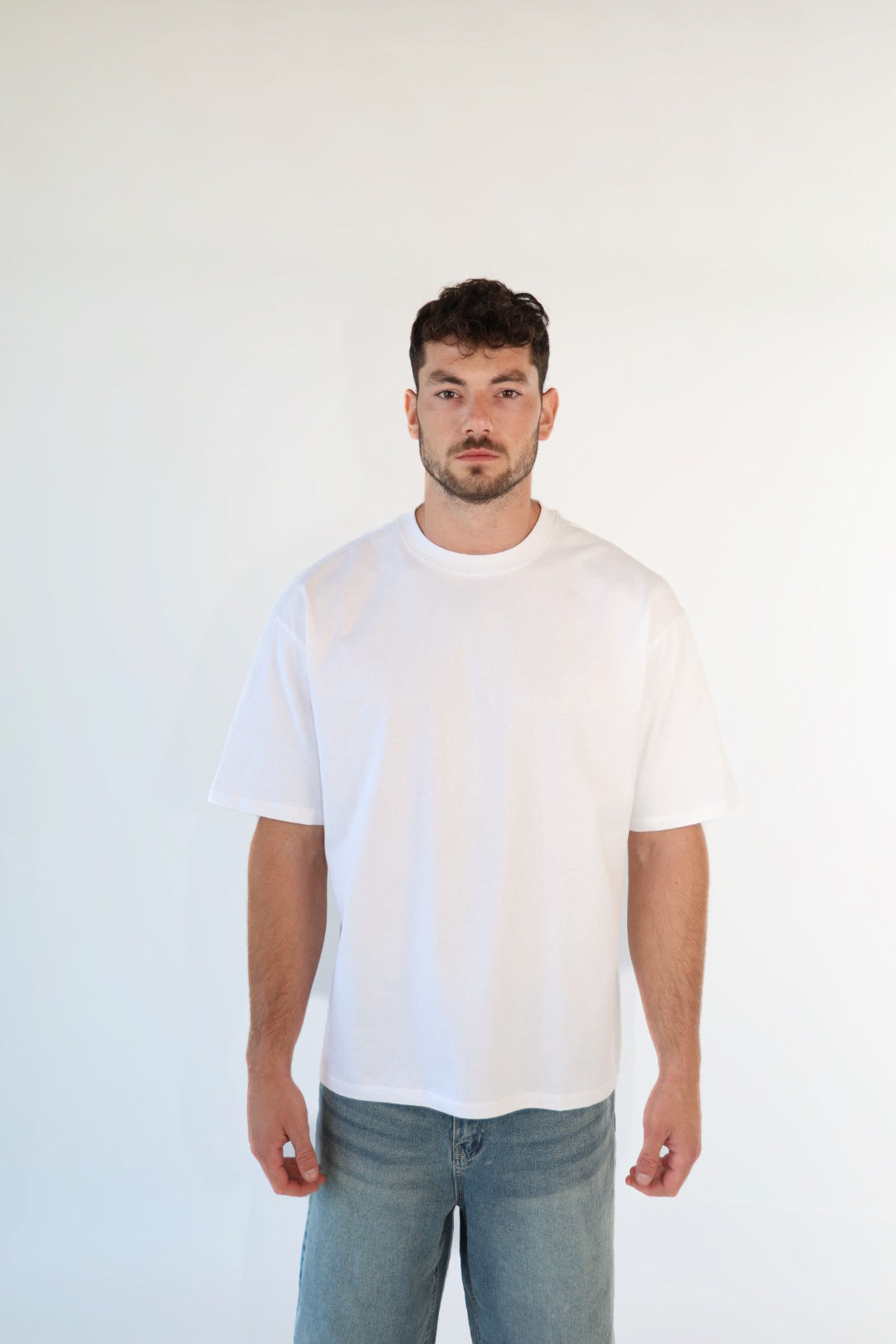 Man wearing a plain white t-shirt and light blue jeans against a white background