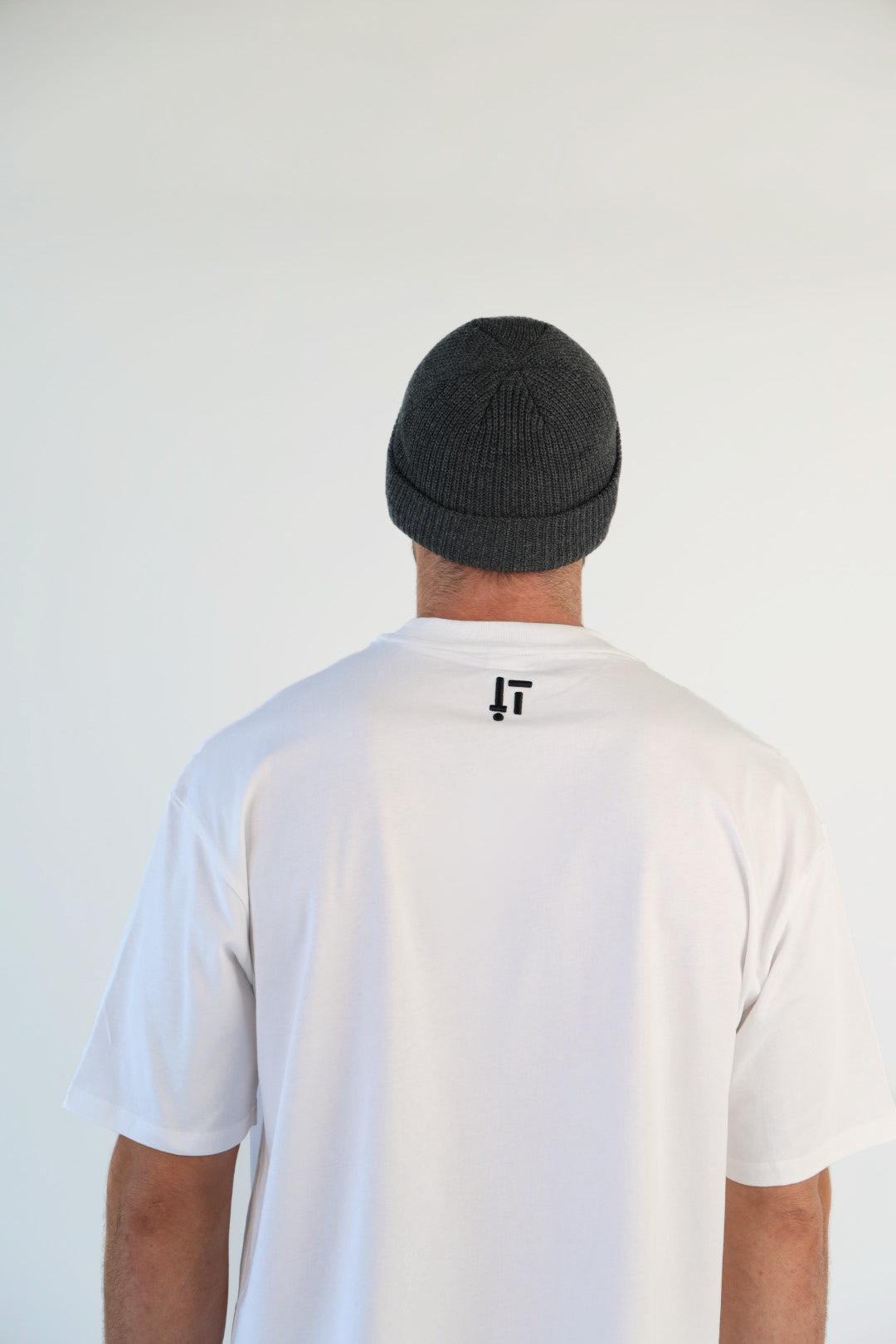 Person wearing a white t-shirt with a logo on the back against a plain background