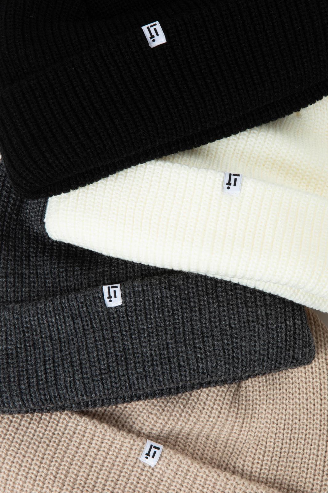 Three beanies in black, gray, and beige with a brand logo on a textured surface.