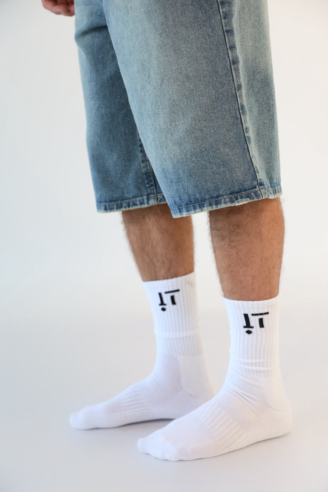 White socks with black logo worn by a person wearing denim shorts on a light background
